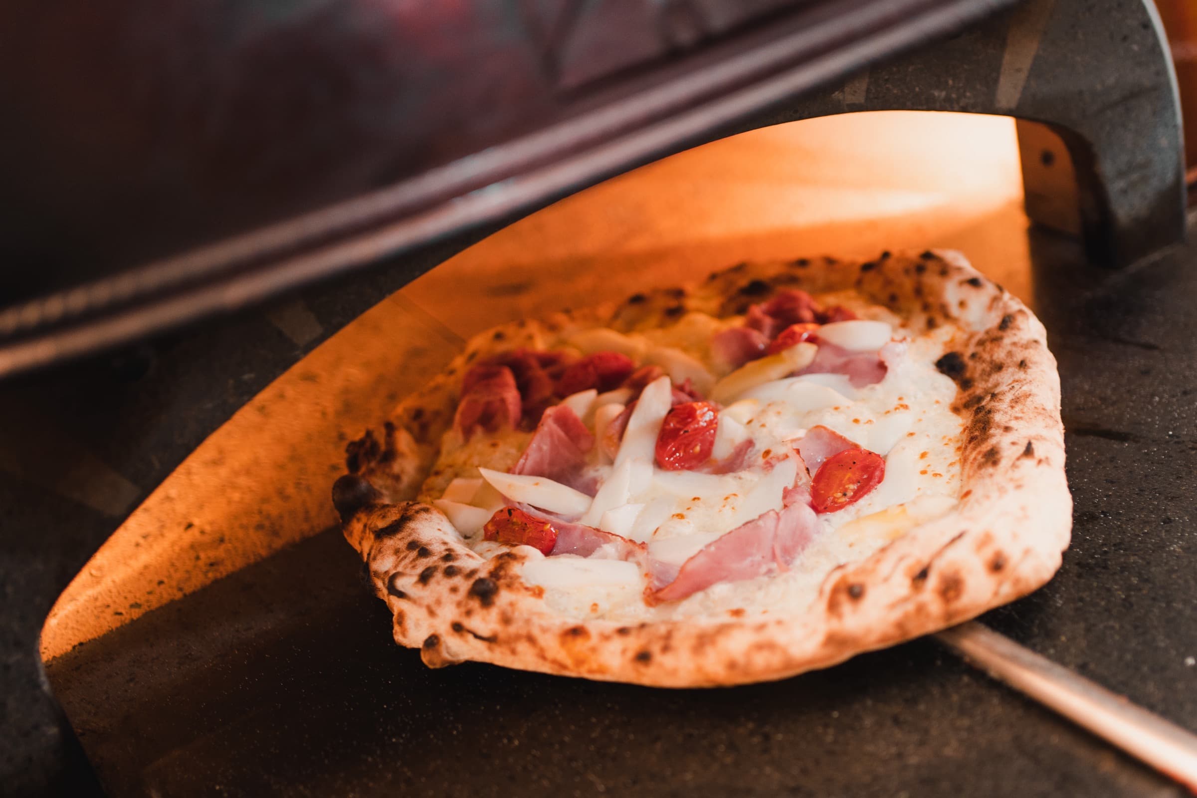 Pizza auf der Schaufel am offenen Holzofen