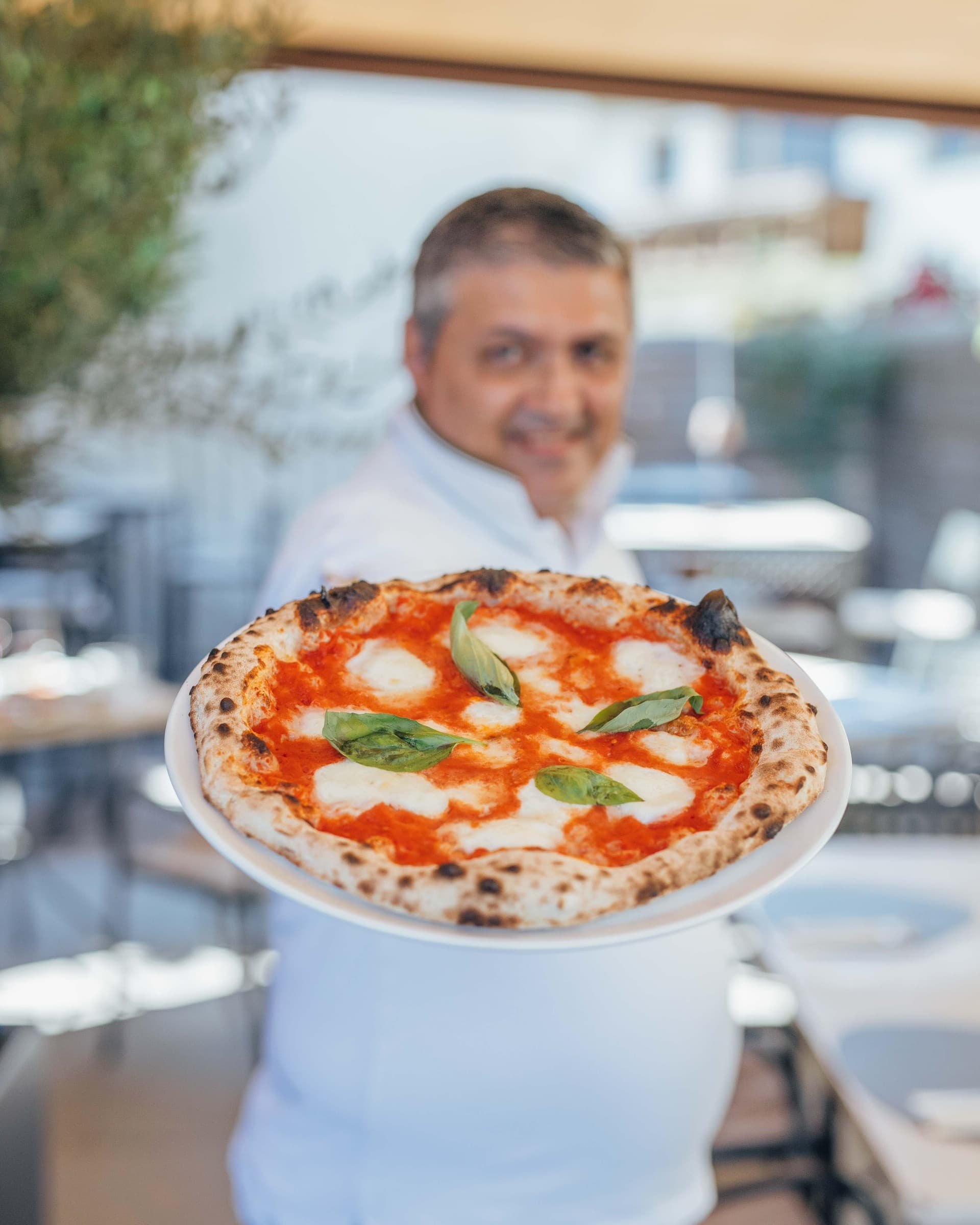 Pizzaiolo hält eine Pizza Margherita in die Kamera