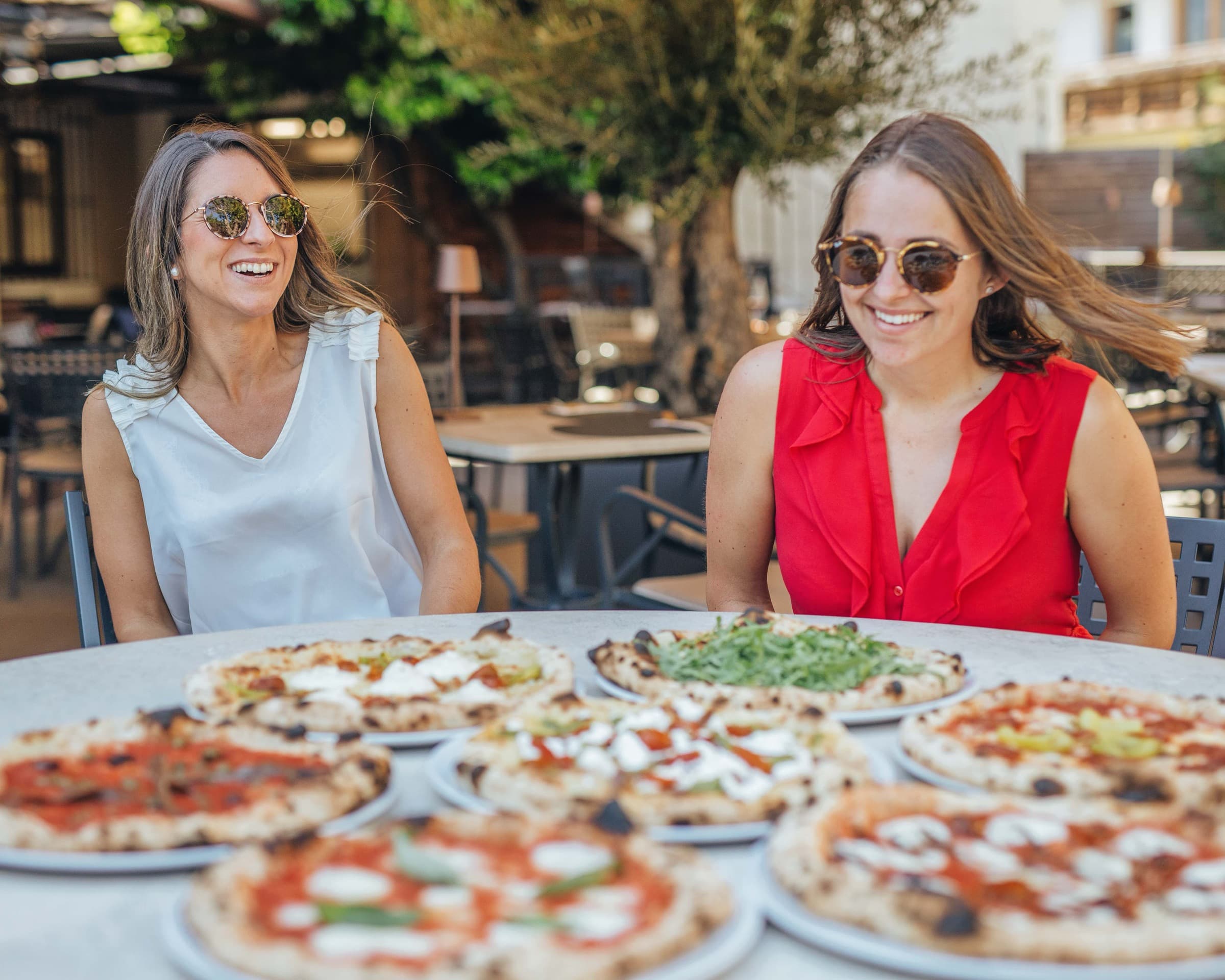 Zwei Gästinnen am Tisch mit sechs Pizzen auf der Terrasse